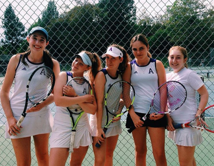 Tennis players, from left to right, Elyse Pollack 18, Liadan Solomon 17, Zoe Woolf 19, Rachel Ferrera 18 and Isabella Simanowitz 18 smile at a match. The teams overall record is  7-4. Photo courtesy of Simanowitz.