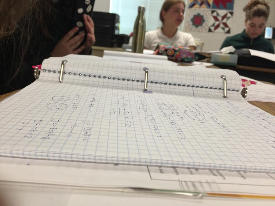 A binder sits on a desk in Leila Chakravartys math classroom. Her ninth and 10th grade Integrated Math III class completes practice problems on solving quadratic and linear systems of equations. 