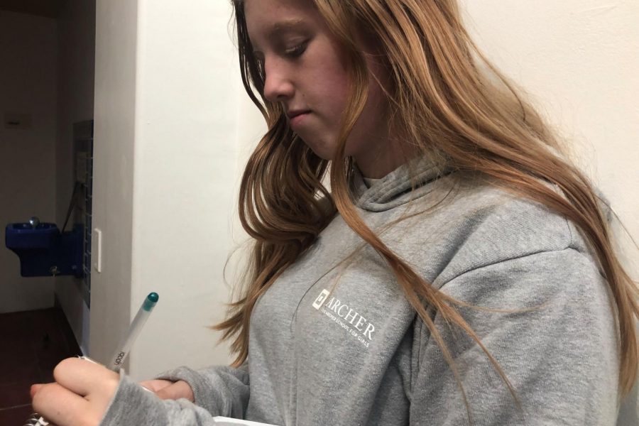 Archer sophomore and singer-songwriter Gwendolyn Hanson writes down song lyrics on a notepad in the Archer art hallway. Her album, which comes out on June 26, will be available on Spotify, Apple Music and Soundcloud. 