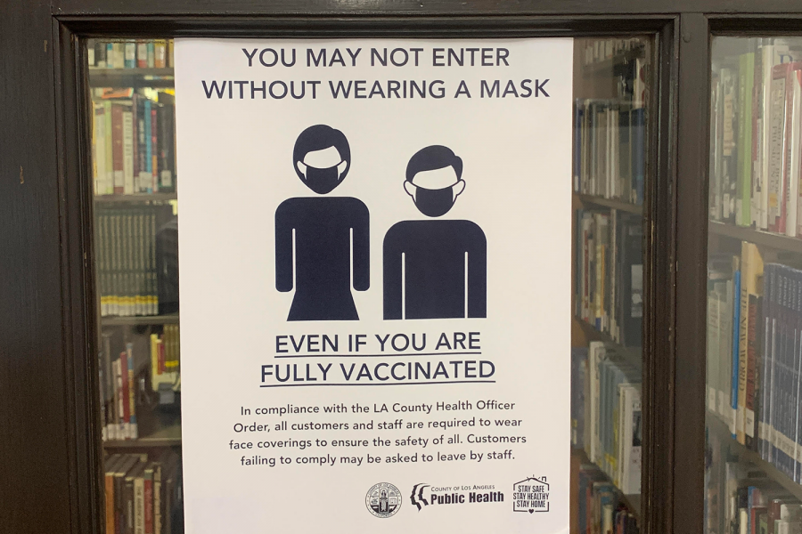 A sign reminding community members to obey masking protocols is displayed on the door of the library. Other signs like this instructing students, faculty, staff and visitors to follow health and safety protocols in order to prevent the spread of COVID-19 are displayed around campus.