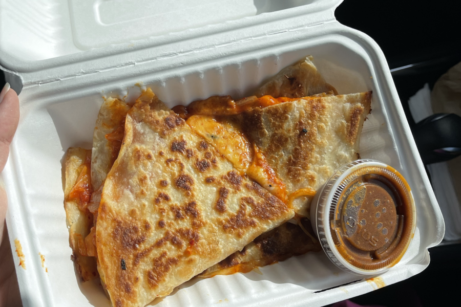 The delicious Kimchi Quesadilla with spicy Korean hot sauce is displayed in the plastic container from the Kogi food truck. This meal combines the perfect blend of the cheesy Mexican classic, and the refreshing Korean household staple.