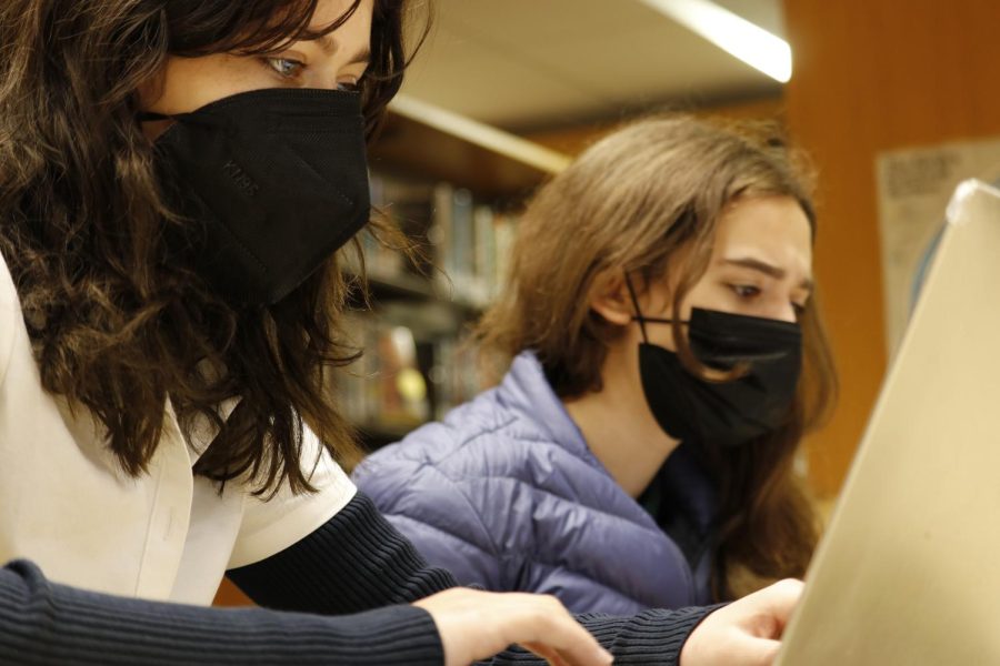 Freshmen Lili Franks and Cezanne Silverton work on a debate case in the library during their first week back from remote learning. Franks is wearing a KN95 mask to take extra precaution against COVID-19. Students have continued the normal school schedule since the return to campus; however, they have to communicate with many classmates online who have had exposure or infection to COVID-19.