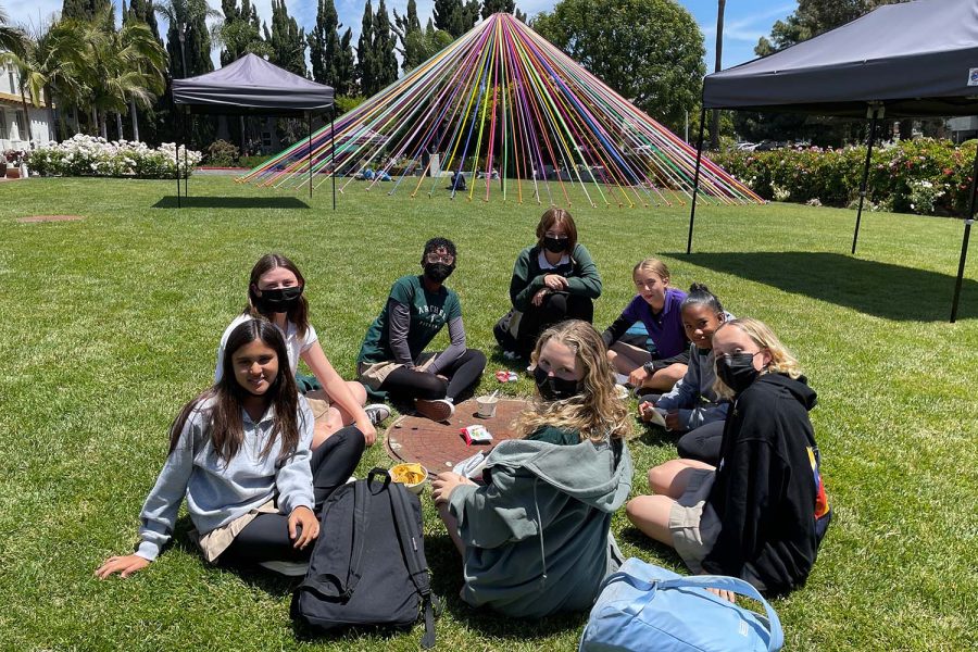 A group of seventh grade students sit in the sun on the front lawn during lunch. The group originally began sitting there when one of them decided to use the drain cover as a makeshift table. 