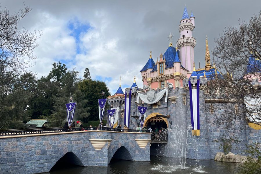 Platinum and purple banners, along with a sliver crest reading Disney 100, adorn Sleeping Beauty Castle while fountains spray out of its moat. The decor is displayed in honor of the Walt Disney Companys 100th anniversary celebration, which began Jan. 27.