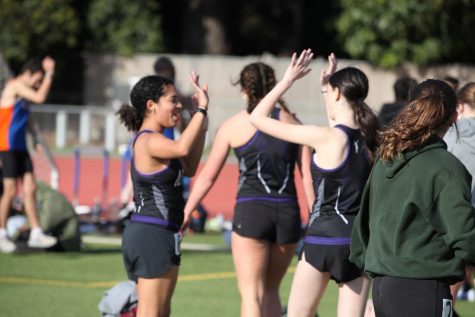  Junior Kayla Bruce a high fives their teammate Mia Vosicher (25) at the University Tri-Meet. Although there were many new teammates this season, Bruce said varsity and track and field members have “built a community with each other in a short time.” 