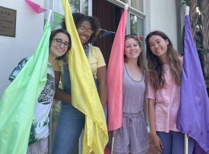 Sophia Bratman (24), Anaiya Asomugha (24), Ella Gray (24) and alumni Ava Cherniss (23) wave colorful flags in the courtyard. They were all counselors for Archer Summer, a paid position where they oversaw group activities with kids and organized camp life.