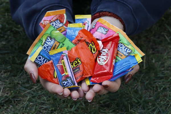 Hands hold halloween candies packaged in non-recyclable wrappers. Opting to purchase candies packaged in compostable or recyclable wrappers is one method of making a beloved Halloween tradition more sustainable. 