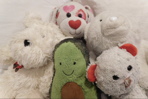 Four stuffed animals and one stuffed avocado are clustered on a bed. A New York Times article stated that stuffed animals help people cope with stress because of the comfort they provide.