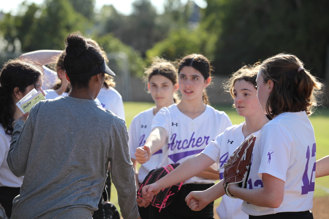 The middle school softball team huddles together with head coach Bre Brown. The team has won all four of their games so far. Photo by Archer Athletics.