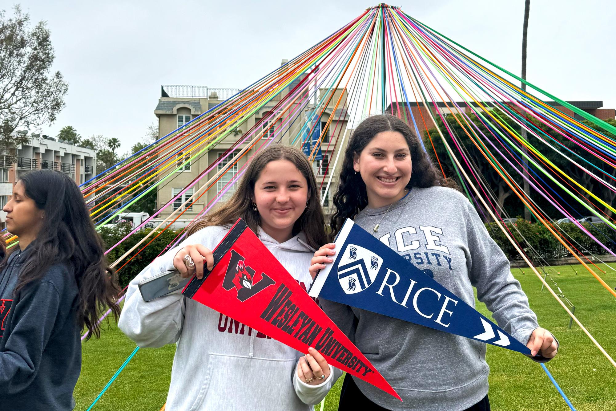 Seniors Annie Friedman and Lilly Dembo stand in front of the Maypole with their college pennants. Archer seniors had their pennant ceremony where they hung up their college pennants in the administration hallway on May 13. (Photo courtesy of Annie Friedman)