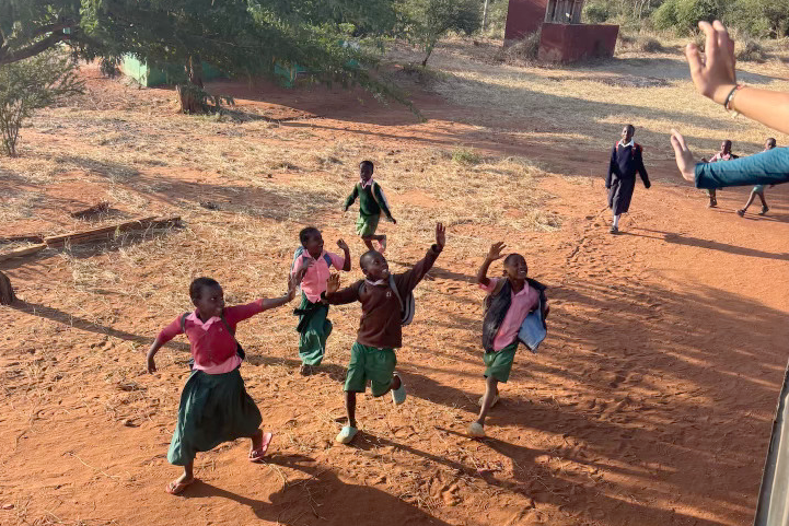 On a dirt road, children run alongside a bus while waving goodbye to Archer students. This past June, upper school students visited Kenya for 11 days through the Archer Abroad program.