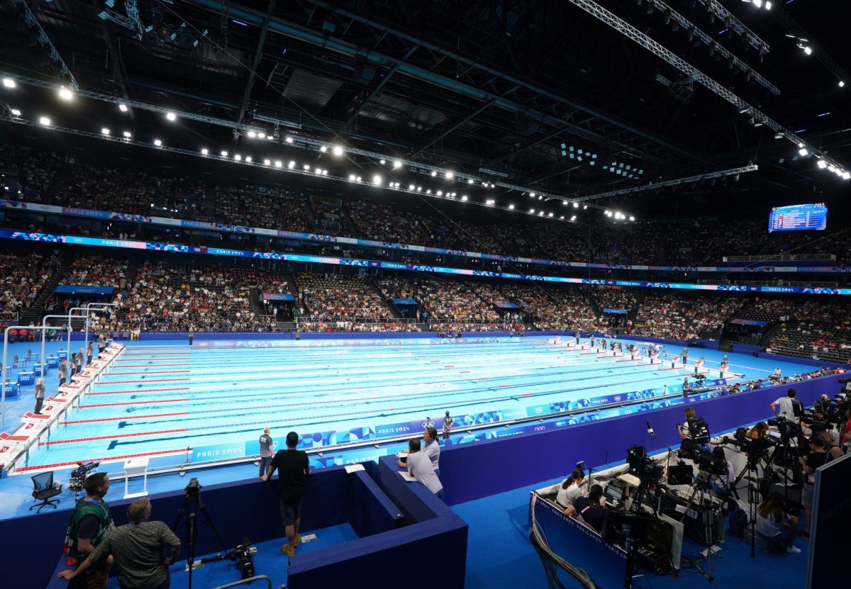 The Paris 2024 Olympic swimming pool is filled with bright lights and spectators. The Olympic games were held from July 26 to Aug. 11. While the event is meant to symbolize global unity, athletes from non-Western countries were met with accusations and scrutiny.  [Paris 2024 Olympic Games] by [Roman Koksarov] is licensed under [CC BY 4.0.].