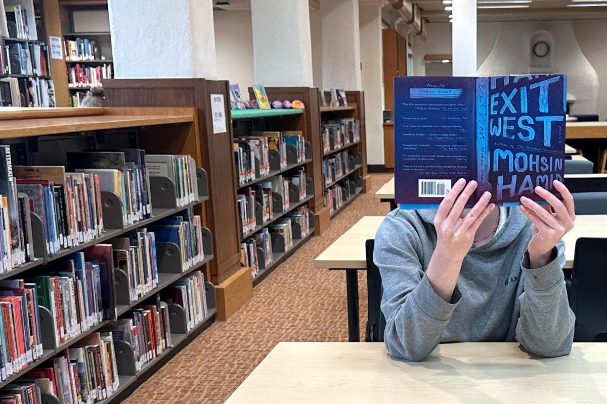 A student reads "Exit West" by Moshin Hamid in the Tia Palermo Library. The novel follows refugees Nadia and Saeed as they emigrate from their home country to the United States through a series of magical doors. 