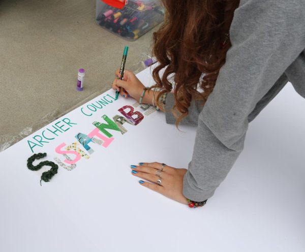 Archer Council for Sustainability member Katia Thomas ('27) writes on the club's poster for the club fair. "We're inspiring our generation to be involved in the environment, because we are the ones who are going to have to improve it," council member Liv Karp ('26) said.