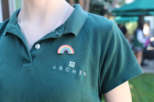 A rainbow pride pin sits beside the logo on an Archer uniform. Vivi Arnold ('26), is a board member on Archer's Gender Sexuality Alliance. Arnold played an integral role in planning the National Coming Out Day celebration.