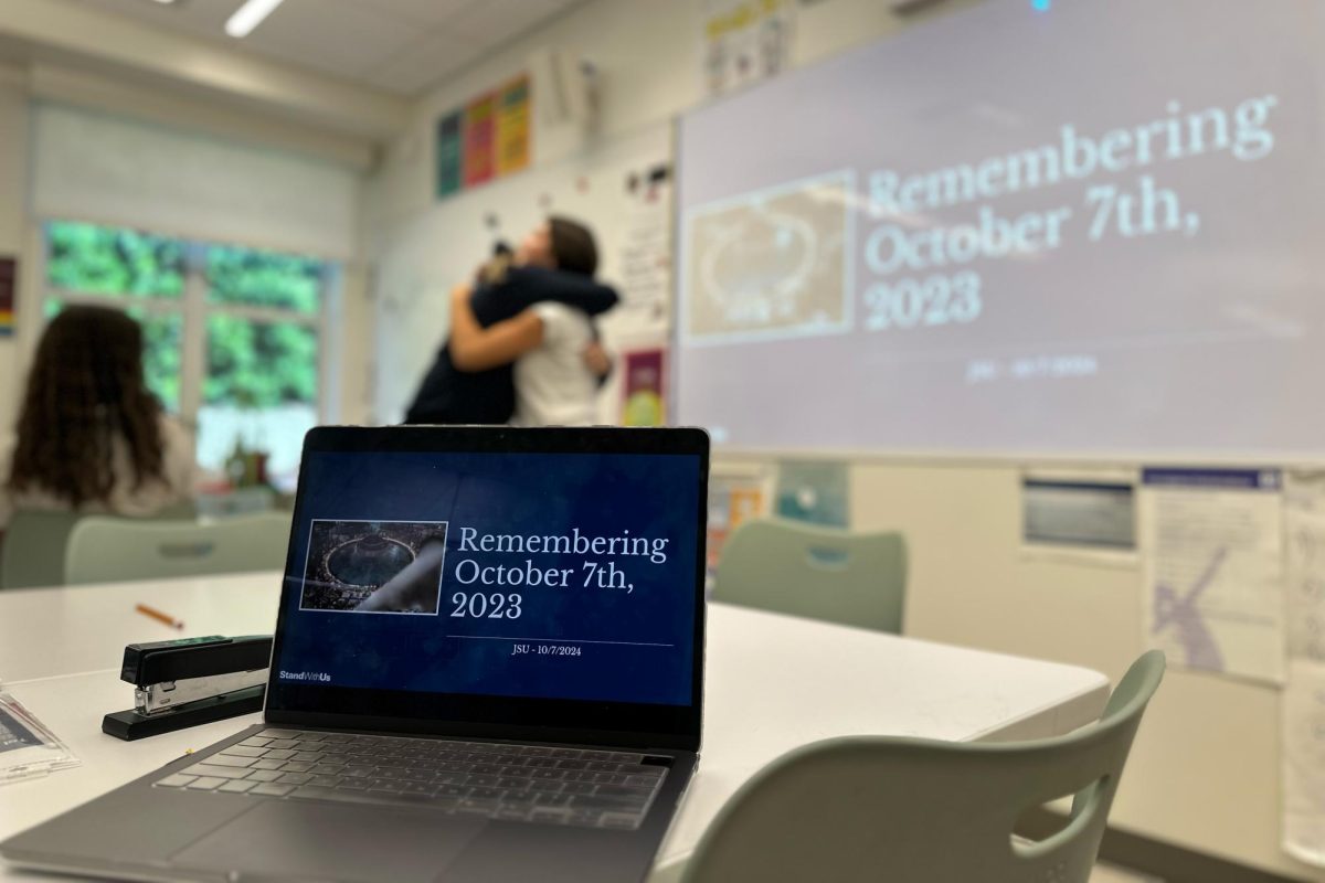 A laptop is open to the opening slide of the Jewish Student Union's Oct. 7 commemoration, as two students embrace in the background. The presentation was one example of how communities in Archer and in Los Angeles came together to recognize the anniversary of the war in Israel and Palestine. 