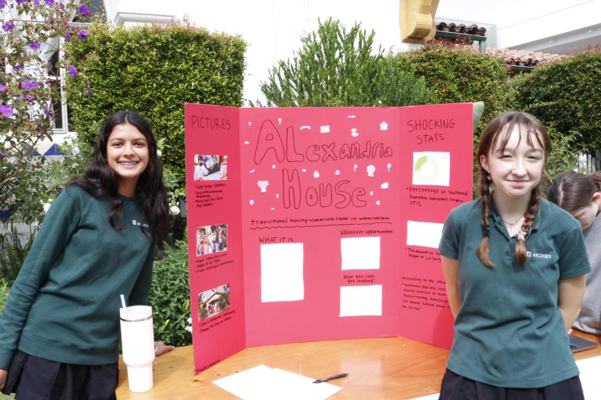 Sophomores Beatrice Washburn and Shanthi Seth stand in front of their poster for the Alexandria House, a women's shelter in Los Angeles. Students from grades 10-12 showcased the service and activism projects at the Archer in Action fair Oct. 17.