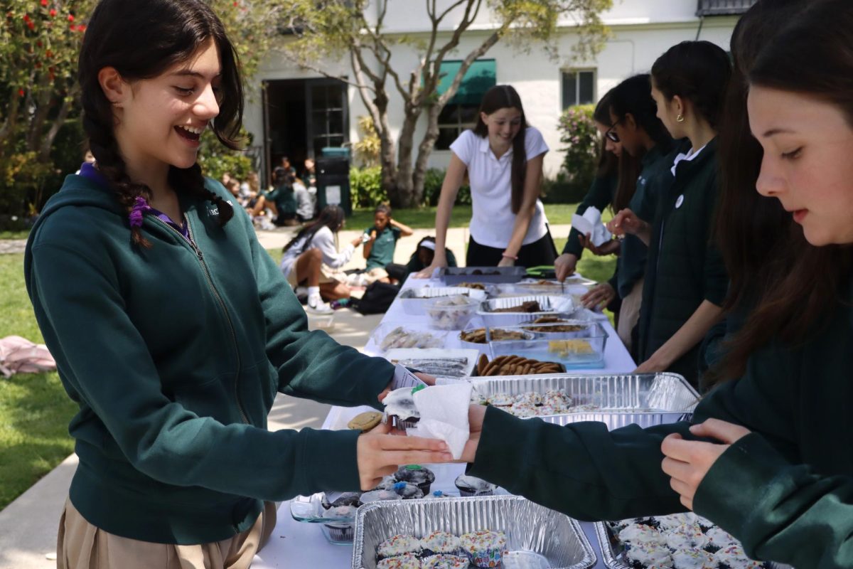 Joey Hansen ('30), a member of the For Goodness Cakes club, hands a cupcake to Lila Berg ('29) during the bake sale April 14. All funds raised by the bake sale will support community outreach initiatives for the For Goodness Cakes organization.