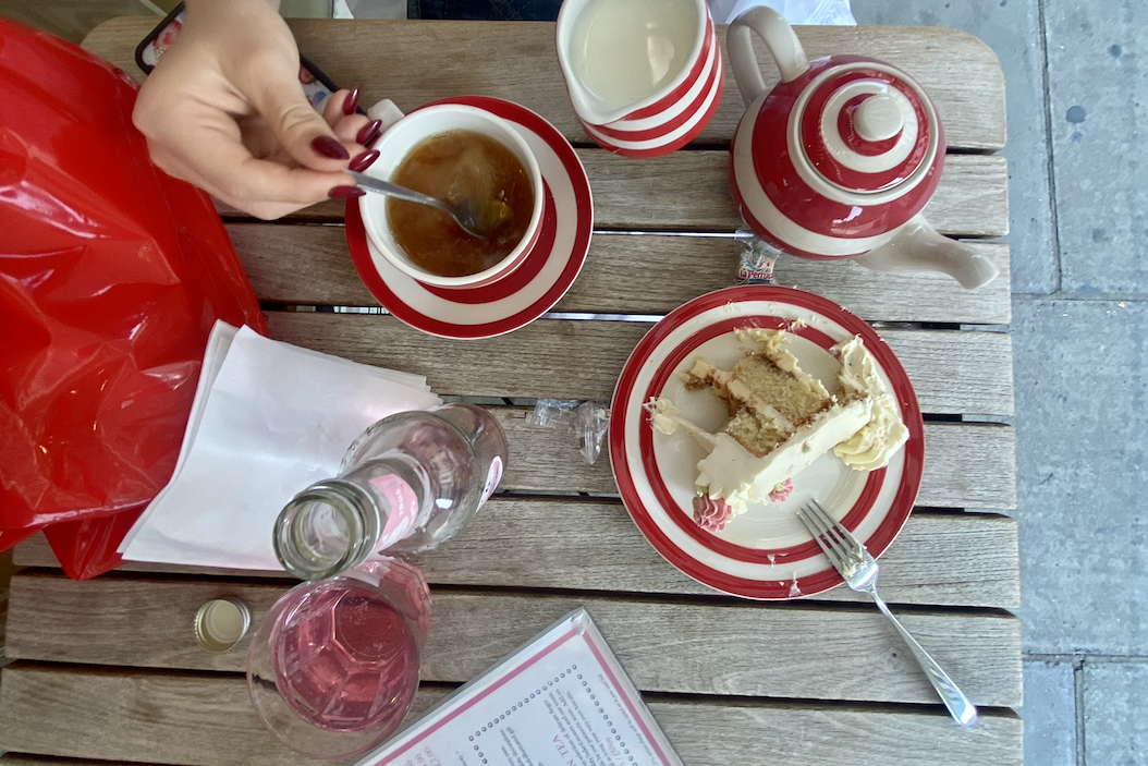 A girl stirs milk into tea, which sits alongside a slice of cake. A quiet pause for a warm beverage can ground us and bring us back into our senses.