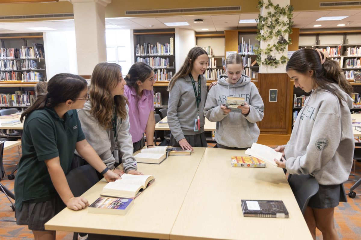 Students gather around a table to discuss a book. During the dystopian-themed Book Tasting in the library, Friday Jan 16, middle schoolers had the opportunity to discover new books. "It was really fun to talk to people about books they had read," seventh grader Allison Levine. said. (Photo courtesy of Amanda Ryvkin.)