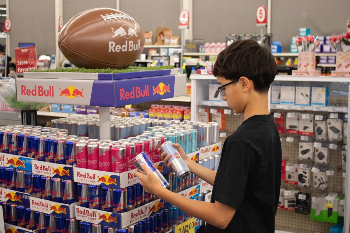 An adolescent stands in front of a Red Bull display in a drugstore, contemplating which flavor to purchase. Studies found that 30%-50% of teens consume energy drinks. However, these highly-caffeinated beverages can have profoundly negative effects on teens’ health and should not be consumed frequently, if at all.