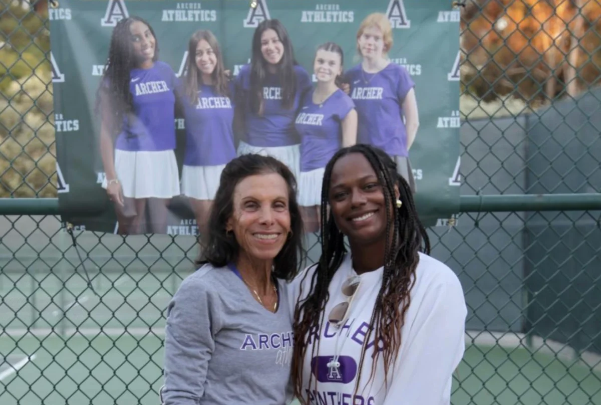 Archer tennis coaches Paula Feigenbaum and Celia Quintero stand in front of a poster with the 2025 Archer seniors on it. Feigenbaum has been Archer's head coach for 10 years and coaches all of Archer's tennis teams.
