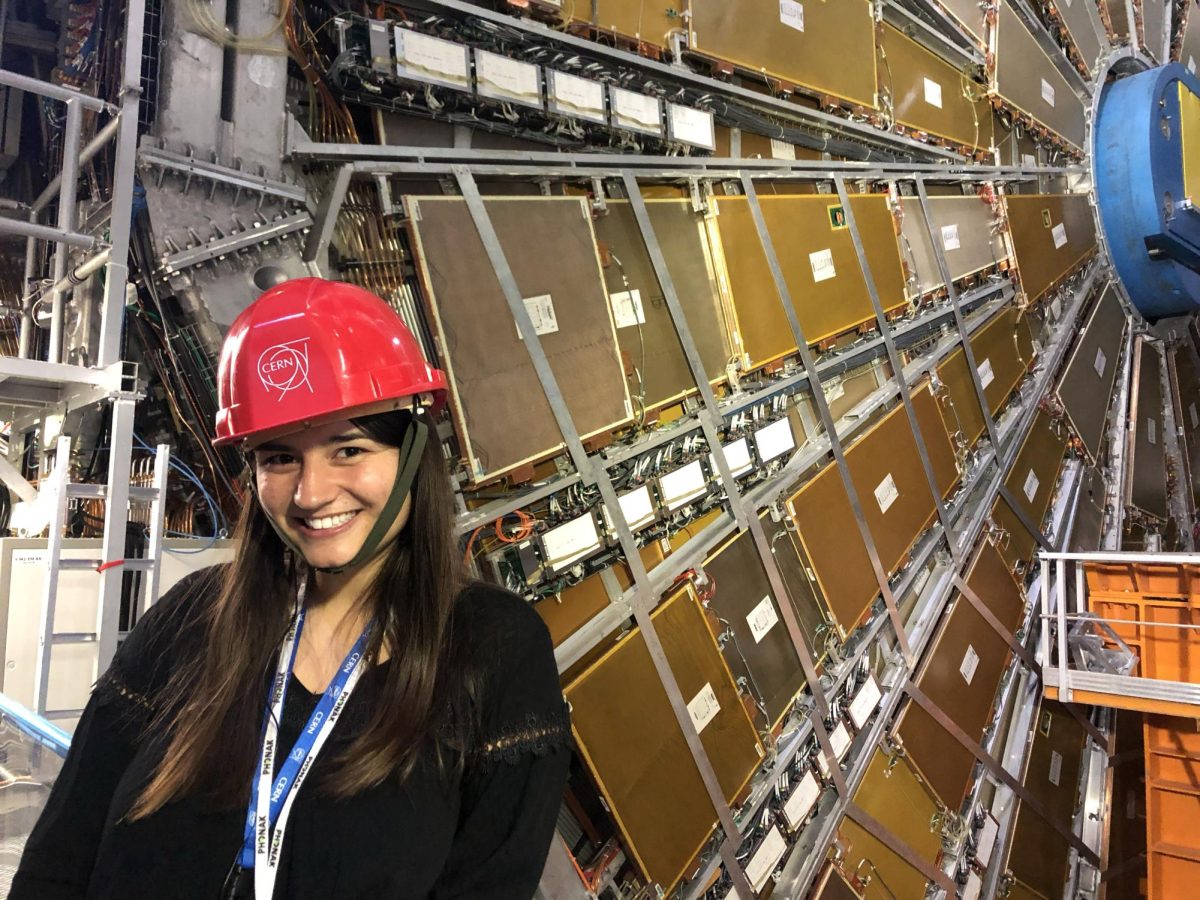 UCLA graduate student Sydney Feldman stands in front of the Large Hadron Collider located in Geneva, Switzerland. It is the world’s largest particle accelerator that pushes protons or ions to near the speed of light. Feldman said she took her first particle physics class as a high school freshman, and it sparked an interest that she has pursued ever since. (Photo courtesy of Sydney Feldman)