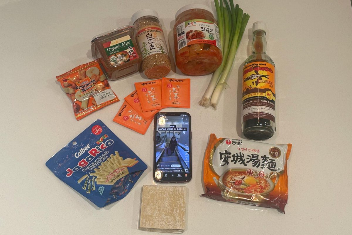 A variety of authentic Asian food and snacks surround a phone playing a video captioned, "Why Japan is living in 2050." There are hundreds of videos such as this on social media that spread stereotypes and false information about Asian countries, that cause harm to those people.