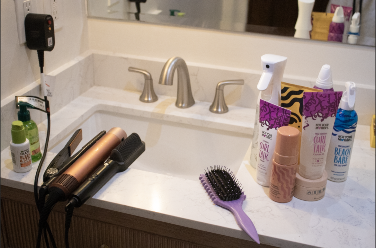 Hair-straightening tools sit alongside natural hair care products on a bathroom counter. This image illustrates the daily choice many people with textured hair face between conforming to beauty standards or embracing their natural hair.