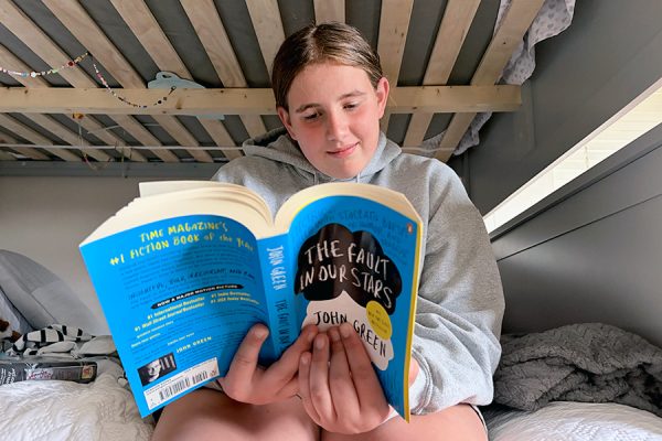A girl sits on her bed and reads "The Fault in Our Stars." The book, written by John Green, follows two teenagers, Hazel Lancaster and Augustus, or Gus, Waters as they navigate a relationship complicated by Hazel's terminal cancer. Green's consistent embrace of Hazel's darker lens of how she sees the world is one of the many elements that made this book excellent.